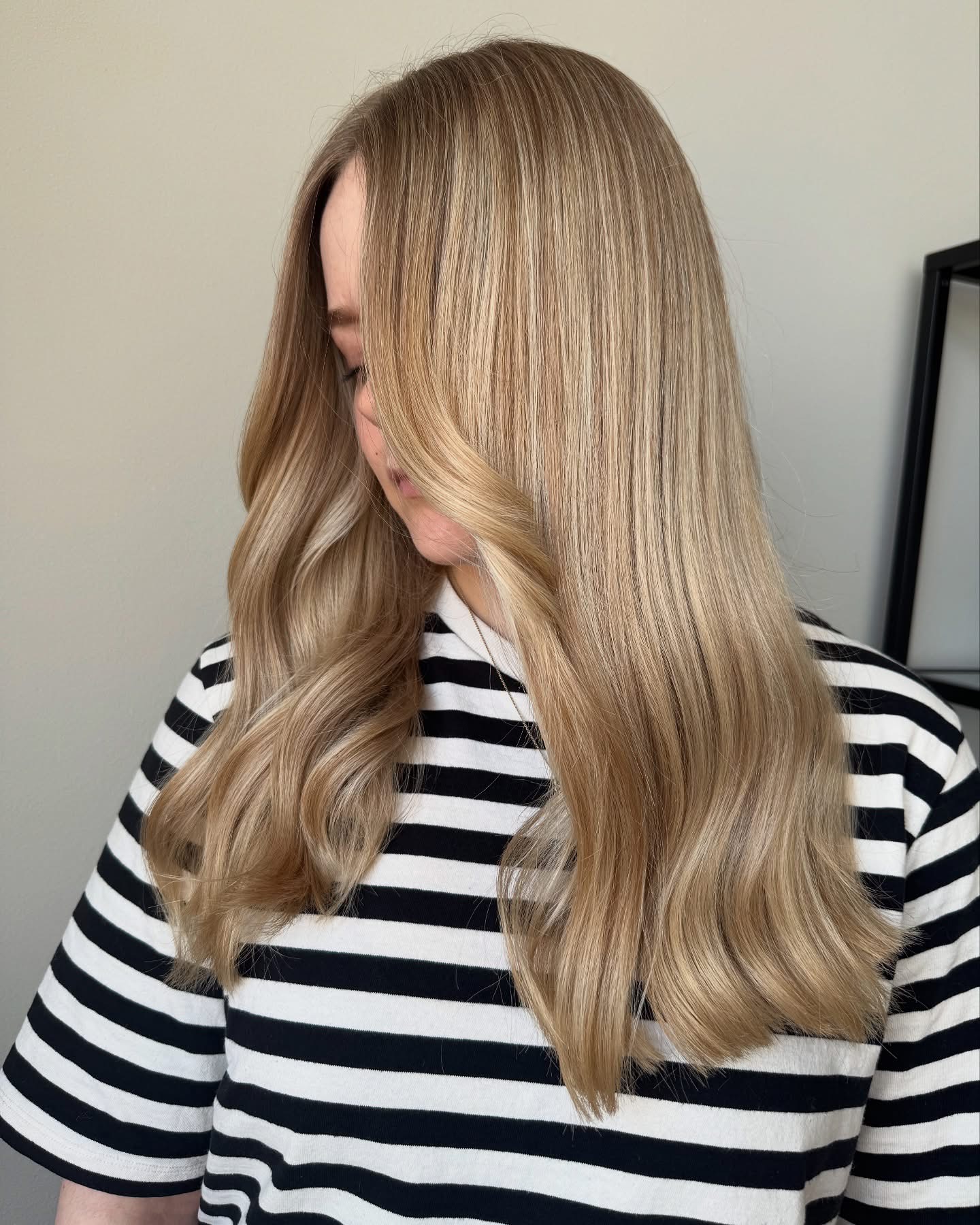 Lang blond haar met balayage en zachte slagen over een gestreept shirt